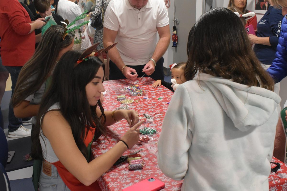 Sophomore, Emely Uriza helping a child make a festive bracelet. 