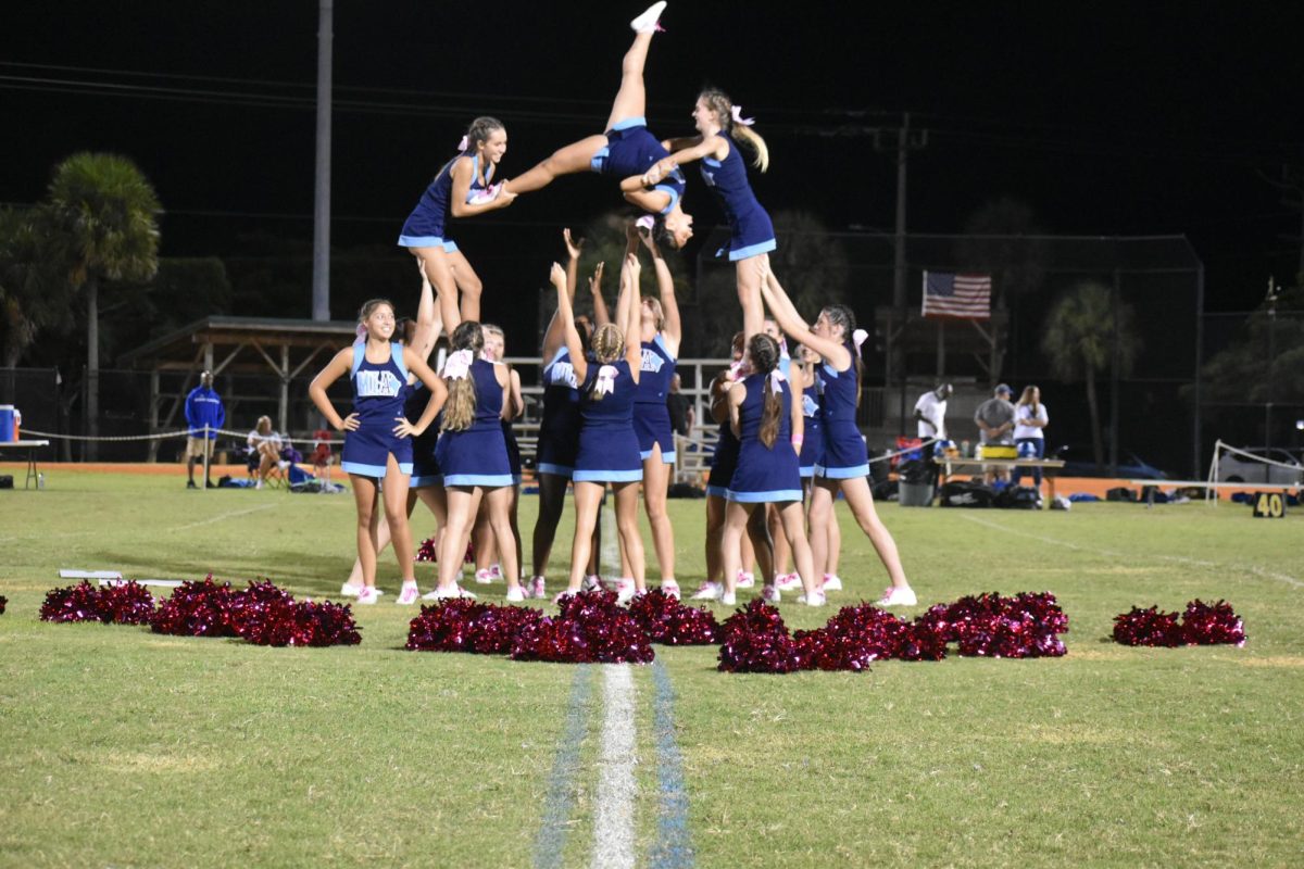 Alyssa Polanco doing a stunt in the air surrounded by the cheer team.