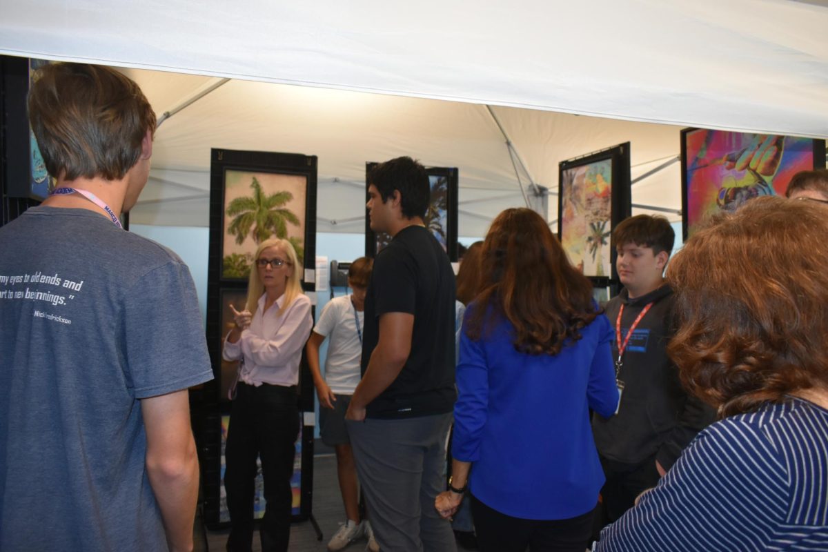 Visitors and students standing in the tent, observing the art. 