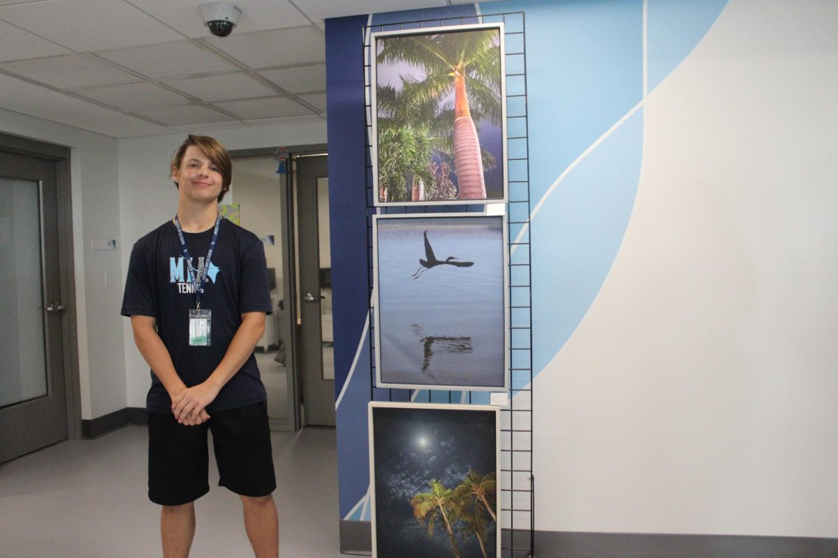 Sophomore Jonathan Juels smiling next to his and others photographs.  