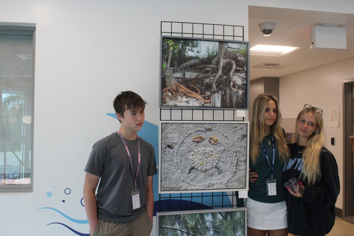 Juniors Adyson Clemens (right), Kaylee Young (far right), and Canon Miller (left) posing next to their photos. 